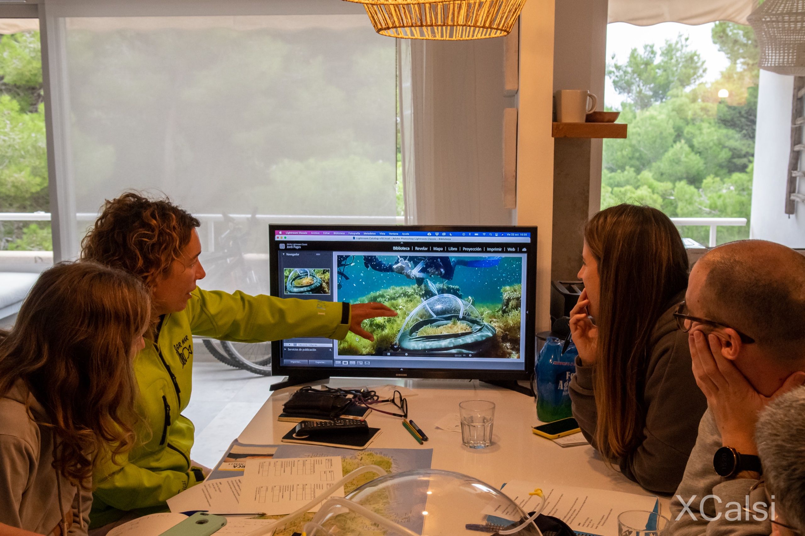 A researcher points at a screen showing an underwater restoration structure during a working meeting